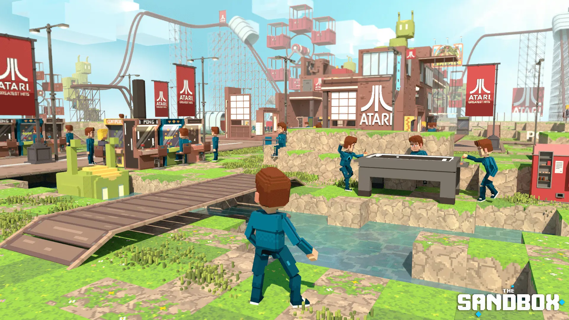 In the game 'The Sandbox', several characters are interacting near arcade machines and banners labeled 'Atari' are visible, set against a colorful pixelated landscape with a bridge over water.